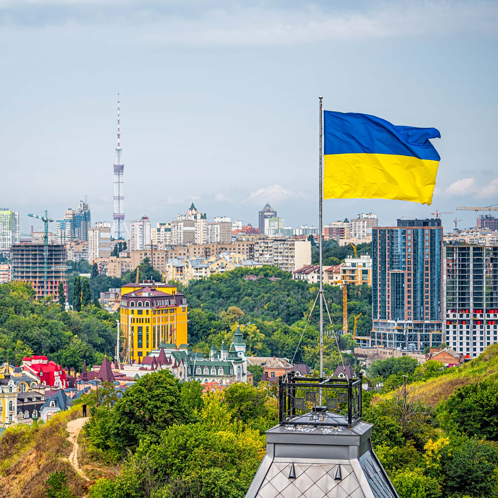 Hazy skyline of buildings in Kyiv, Ukraine. A blue-and-yellow Ukrainian flag flies in the foreground.