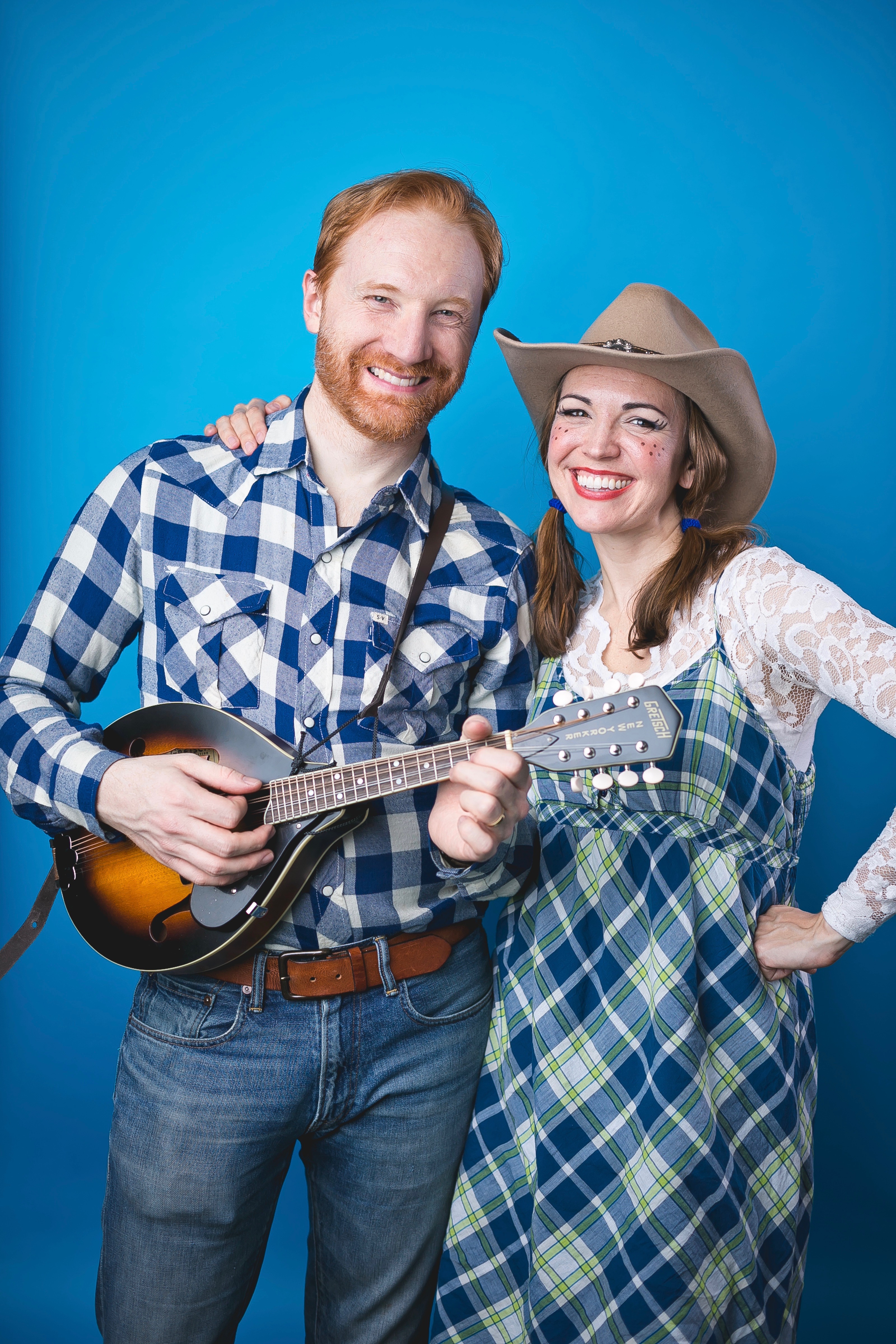 Erik in a plaid shirt holding a banjo and Miss Jamie in a plaid dress and cowboy hat