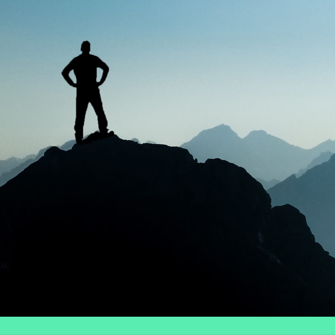 Silhouette of a hiker standing on top of a mountain summit looking triumphant