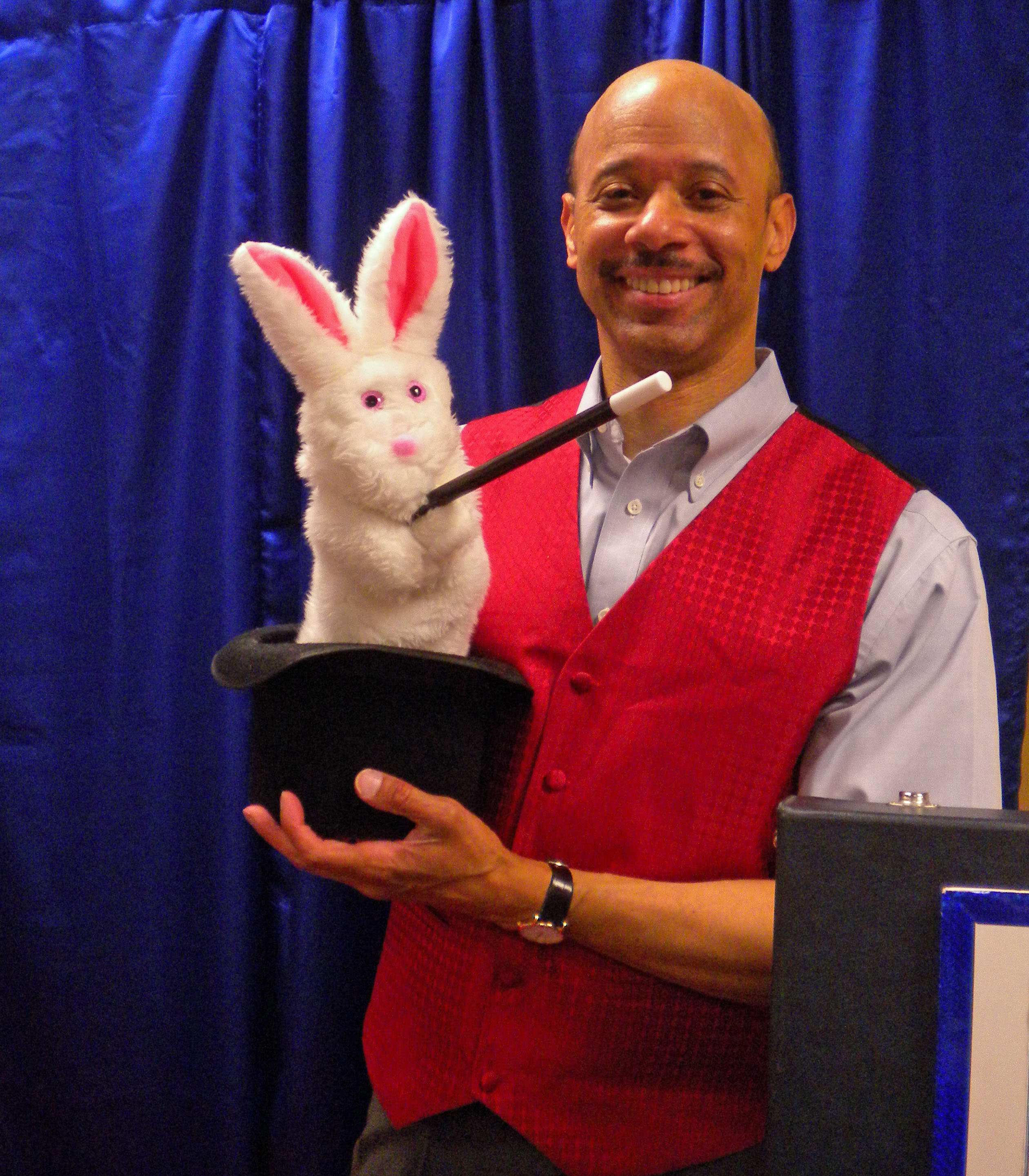 Morris in a red vest holding a rabbit in a top hat