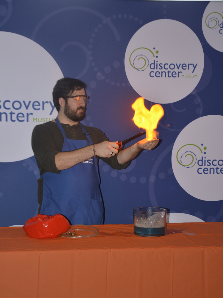man in blue apron with small fire from a bunsen burner