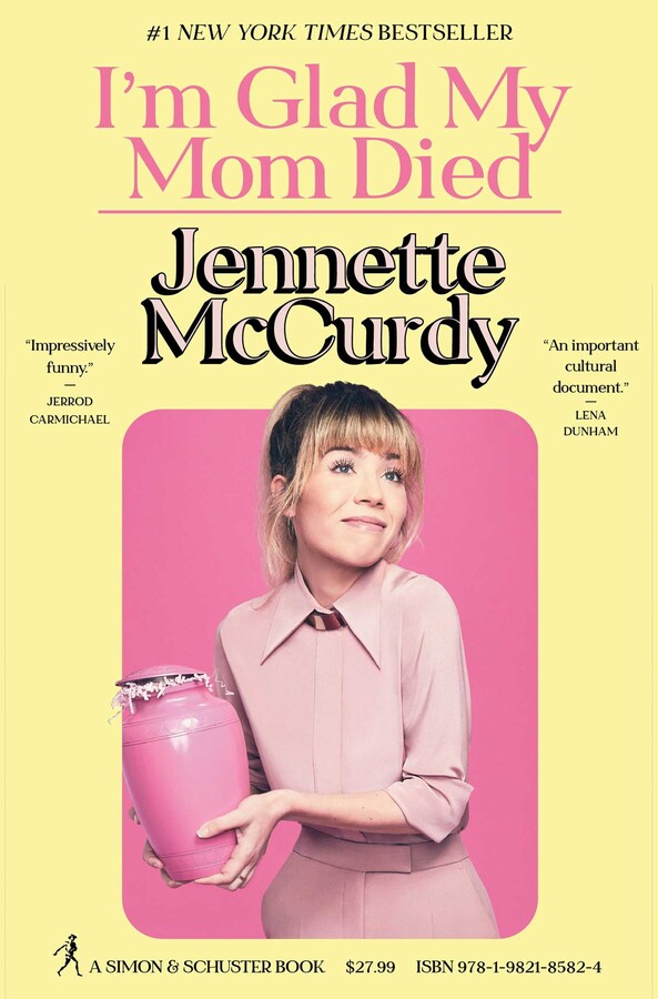 Jennette McCurdy is smiling while wearing a pink suit. She is holding a pink urn. 