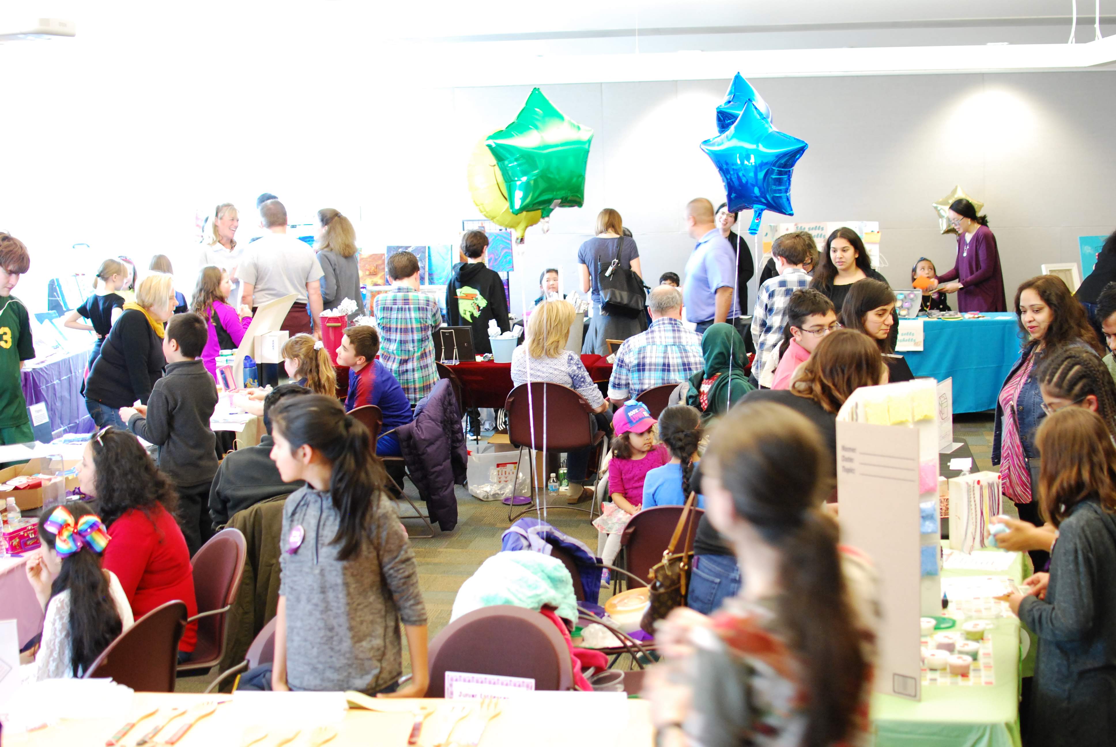 Photo of the meeting room filled with sales booths, kids, shoppers and balloons