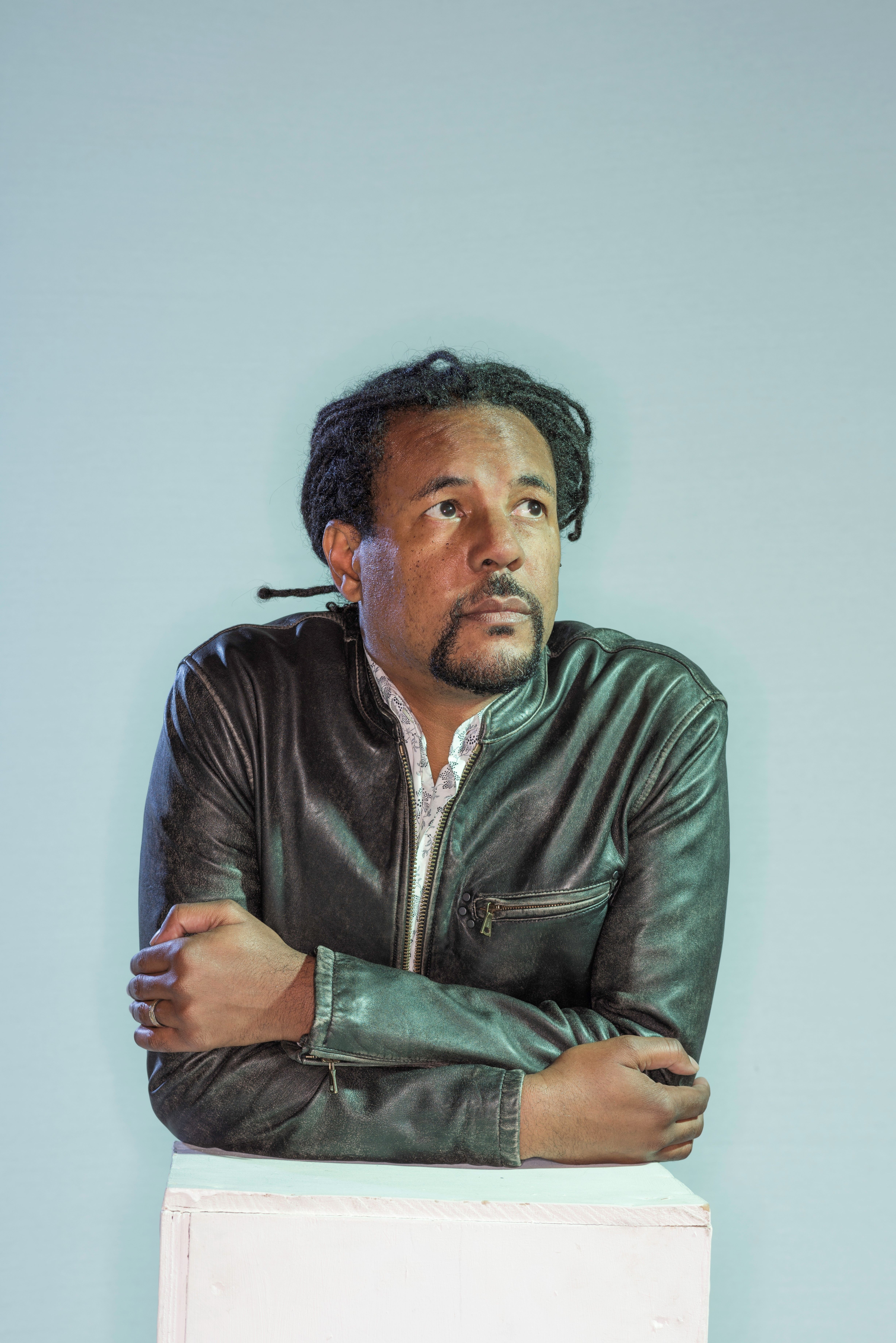 Portrait of Colson Whitehead, a Black man with braids pulled back into a ponytail behind his head. 