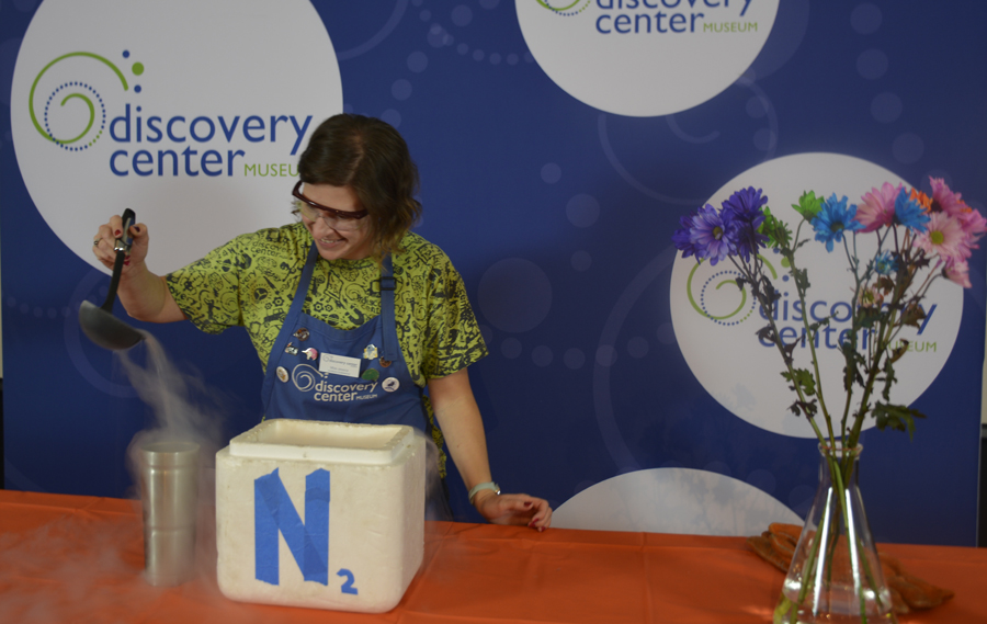 Woman in green shirt and blue apron pours liquid nitrogen into a caontainer