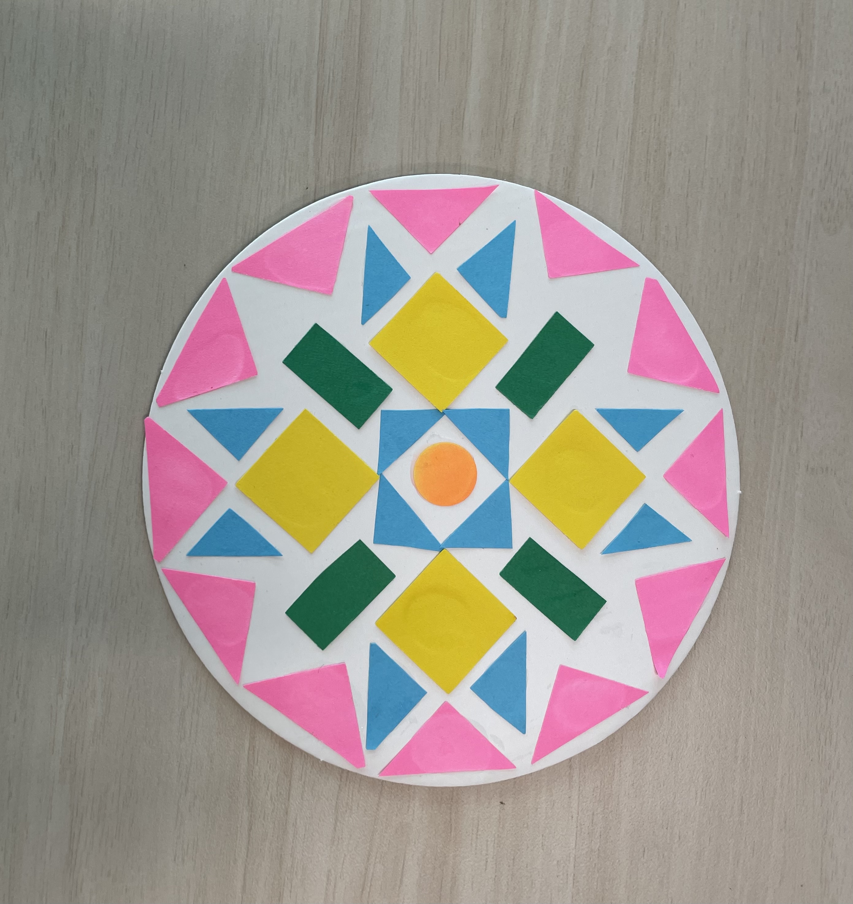 White paper circle with a symmetrical design of colorful triangle and squares.