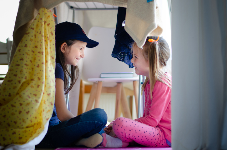 Two children lovingly look at each other under a blanket fort.