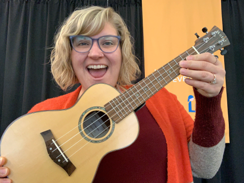A woman holds up a ukulele. She looks excited.