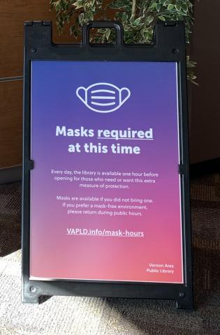 Photo of an a-frame sign in the library lobby. The sign reads "Masks required at this time. If you prefer no mask, come back later."