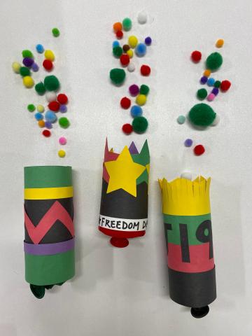 Juneteenth 'poppers' made from a cardboard tube and colored paper. They appear to be launching pom-poms.