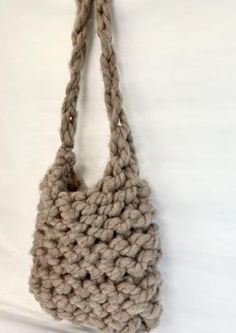 A chunky, hand-crocheted bag on a white background. The bag is gray and has a knit handle.