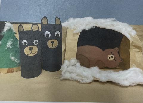 Brown and black bears made out of paper with green paper trees and paper cave