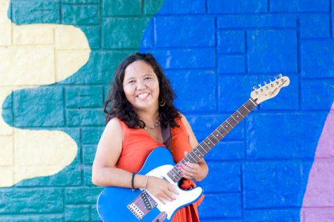 Woman with brown hair in an orange dress holding a blue guitar