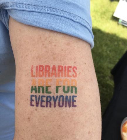 Close up of a woman's arm with a Libraries are for Everyone rainbow tattoo.
