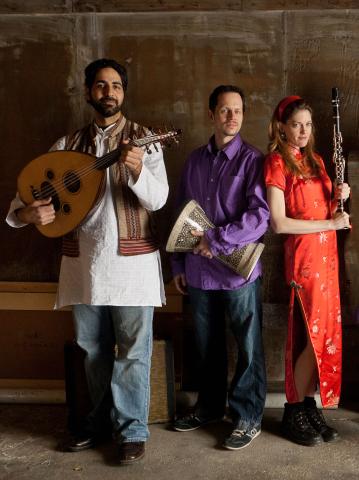 Thee musicians: a tall man with a beard holding an oud (stringed instrument), a shorter man in a purple tunic holding a drum, and a woman in a red silk dress holding a wind instrument