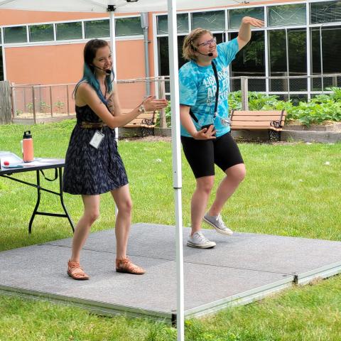 An outdoor stage, upon which are two energetic librarians