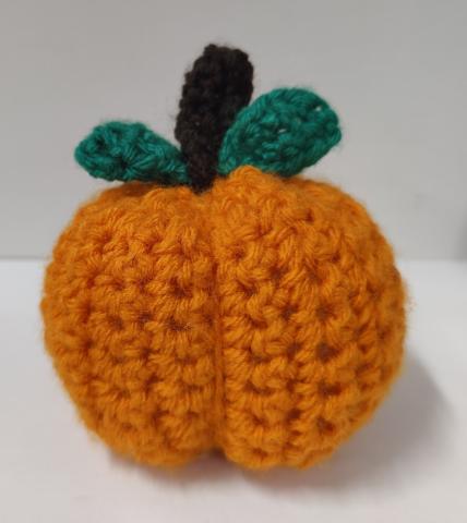 Crocheted oranged pumpkin witha brown stem and 2 green leaves on a white background