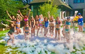 Kids in bathing suits on a lawn full of foam bubbles
