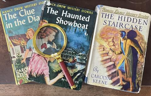 Covers of  three Nancy Drew books with a magnifying glass