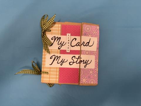 Handmade book with green ribbons ties and pink, purple and yellow strips of paper on a bright blue background