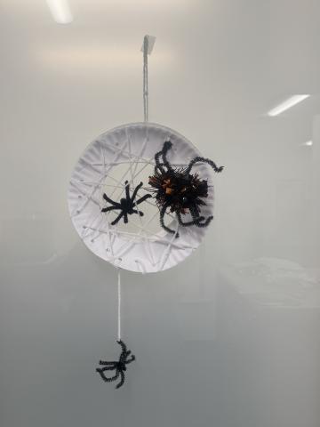 "Spiderweb" made out of a white paper plate and yarn with black spiders made out of pipe cleaners 