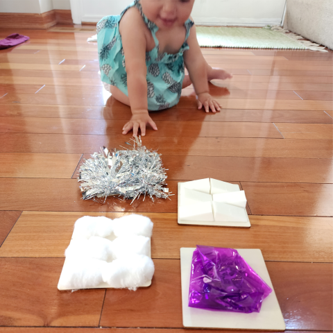 Baby approaches wooden squares with textured items on top