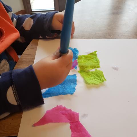 Baby paints a scrap of tissue paper onto a sheet of paper