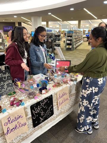 Two students interact with a customer at a sales table with homemade goods
