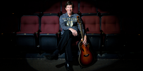 Denny sitting in a theater with a guitar