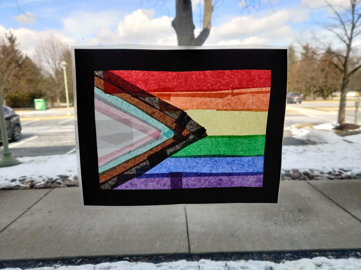 A tissue paper suncatcher on a window in a pride flag pattern