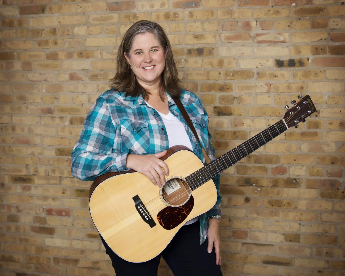 Laura in blue plaid shirt holding a guitar