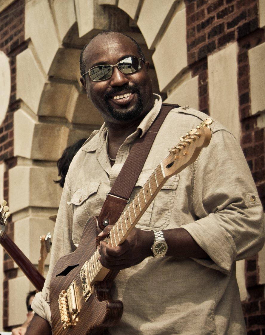 Bill in tan shirt and sunglasses strumming a guitar