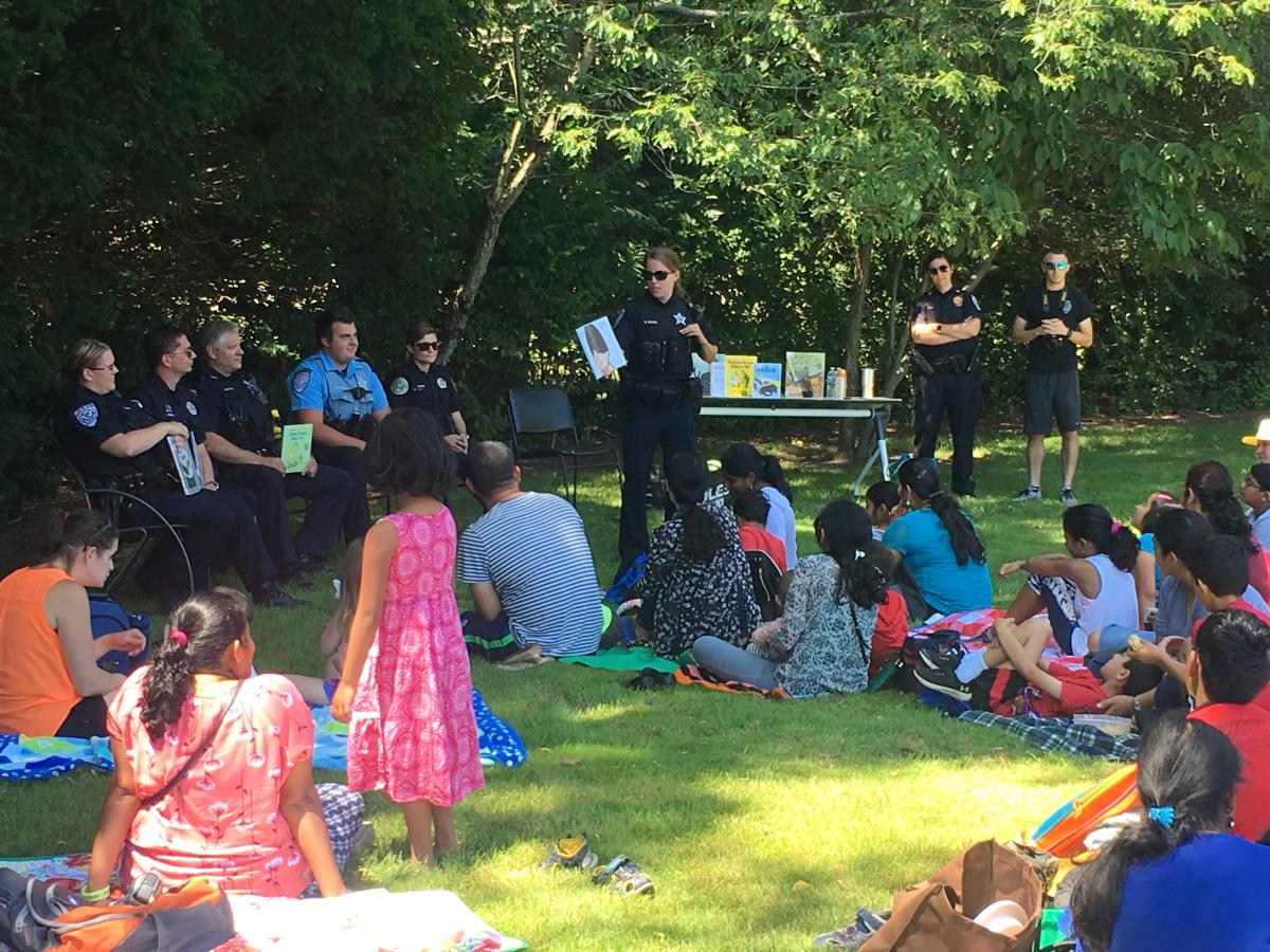 police officers reading stories to families sitting on the lawn.