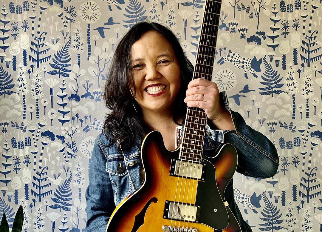 Little Miss Ann in a jean jacket and white pants holding a guitar