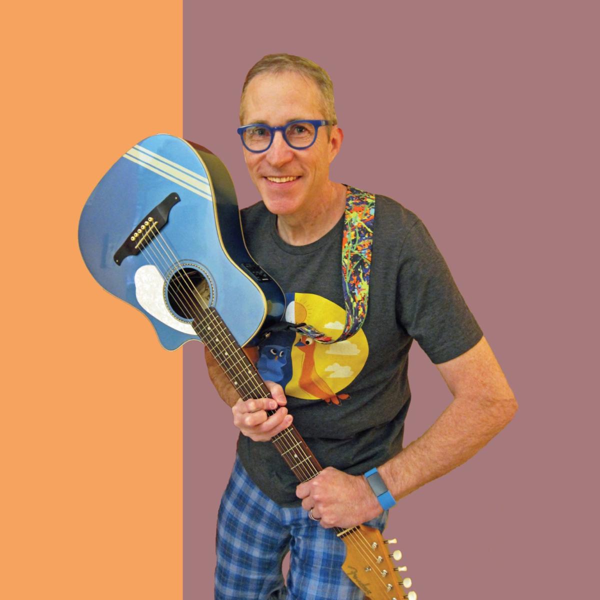 Man in grey t-shirt and glasses holding an upside down blue guitar