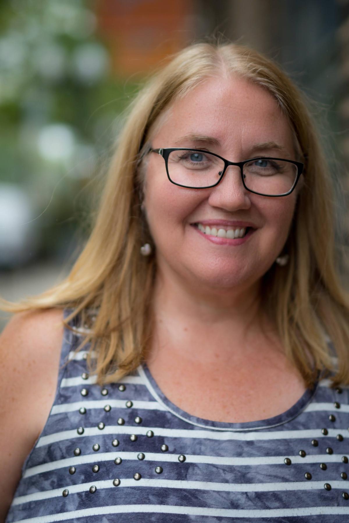 Young woman with blond hair wearing glasses and blue & white striped shirt