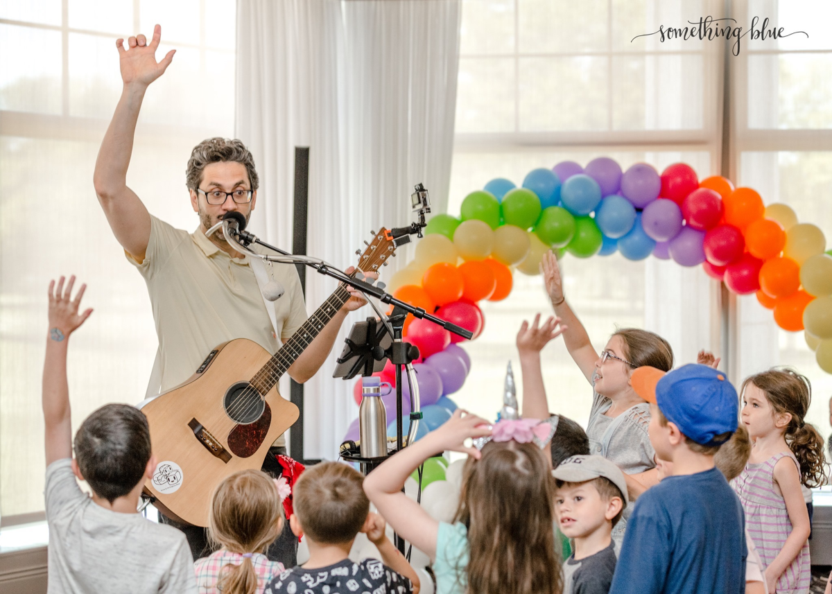 Istvan playing guitar with rainbow balloons and kids in audience