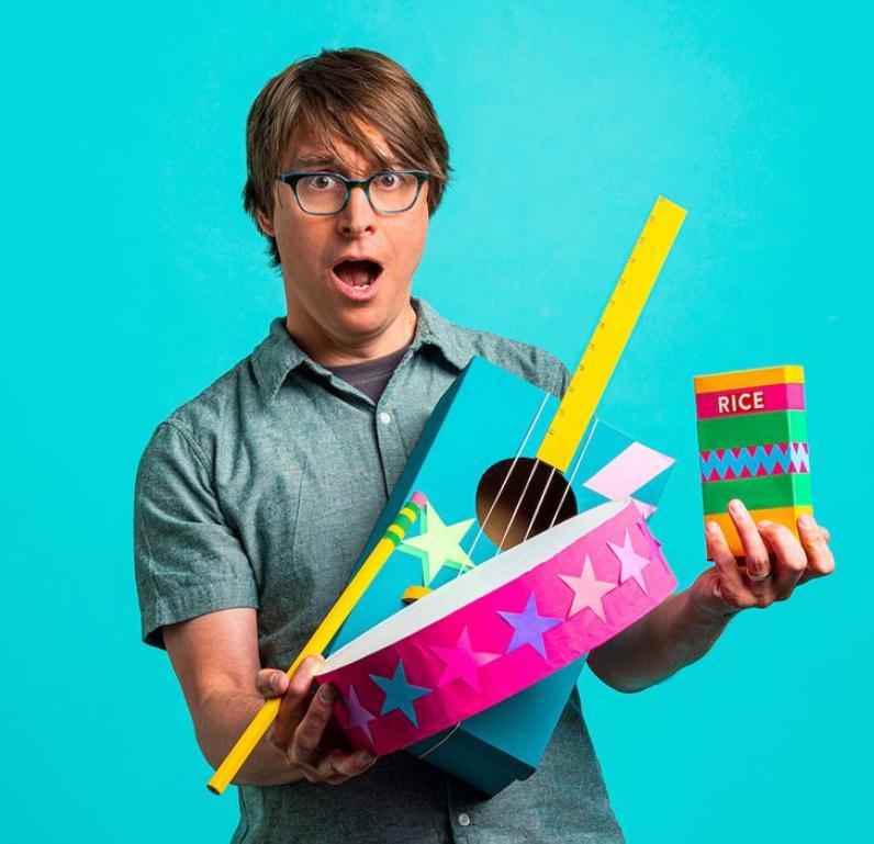 Man in blue shirt and glasses holding pink tambourine and ukulele