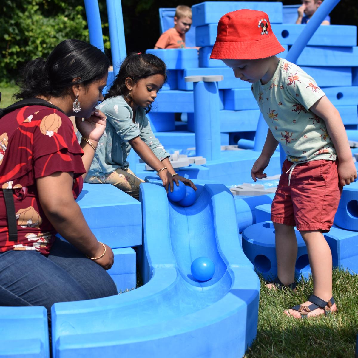 two children playing with big blue blocks with adult watching