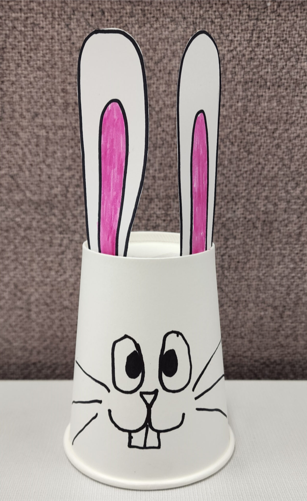 White cup with long ears glued to top and bunny face drawn on the outside.