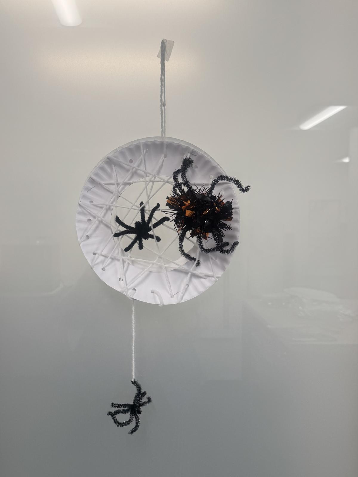 "Spiderweb" made out of a white paper plate and yarn with black spiders made out of pipe cleaners 
