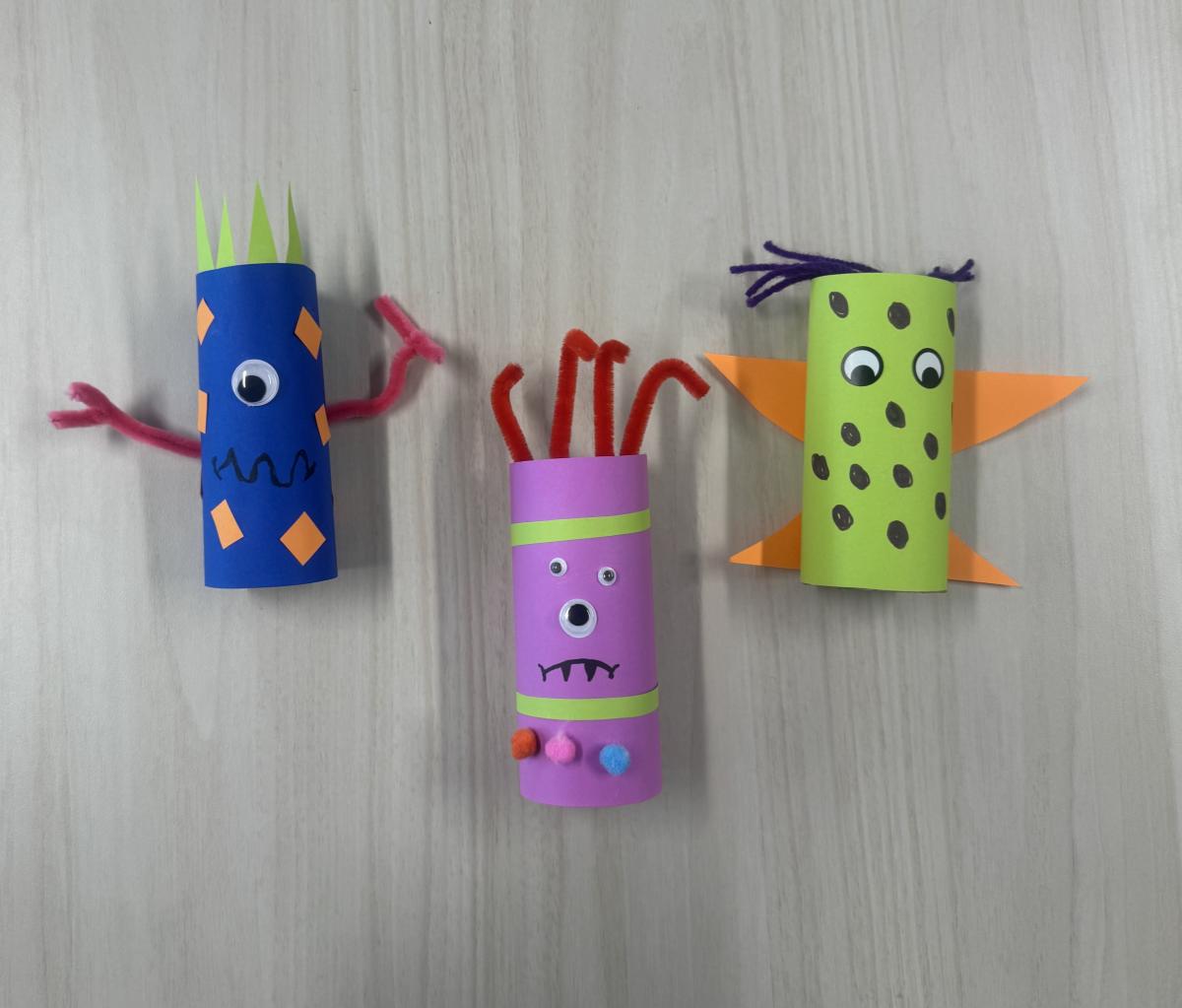 Blue, purple and green paper tube roll monsters with googly eyes, yarn and pipecleaners