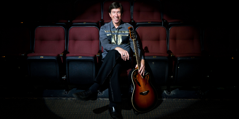 Denny sitting in a theater with a guitar